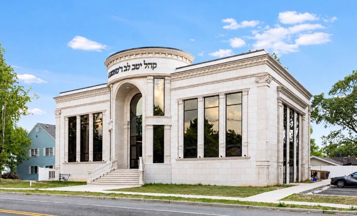 Stone shul exterior with an arched entry and tall black windows